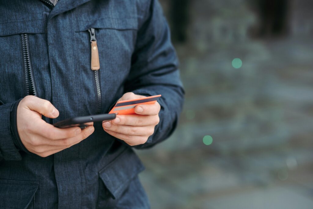 Man holding credit card and browsing smartphone on street indicative of spending culture.